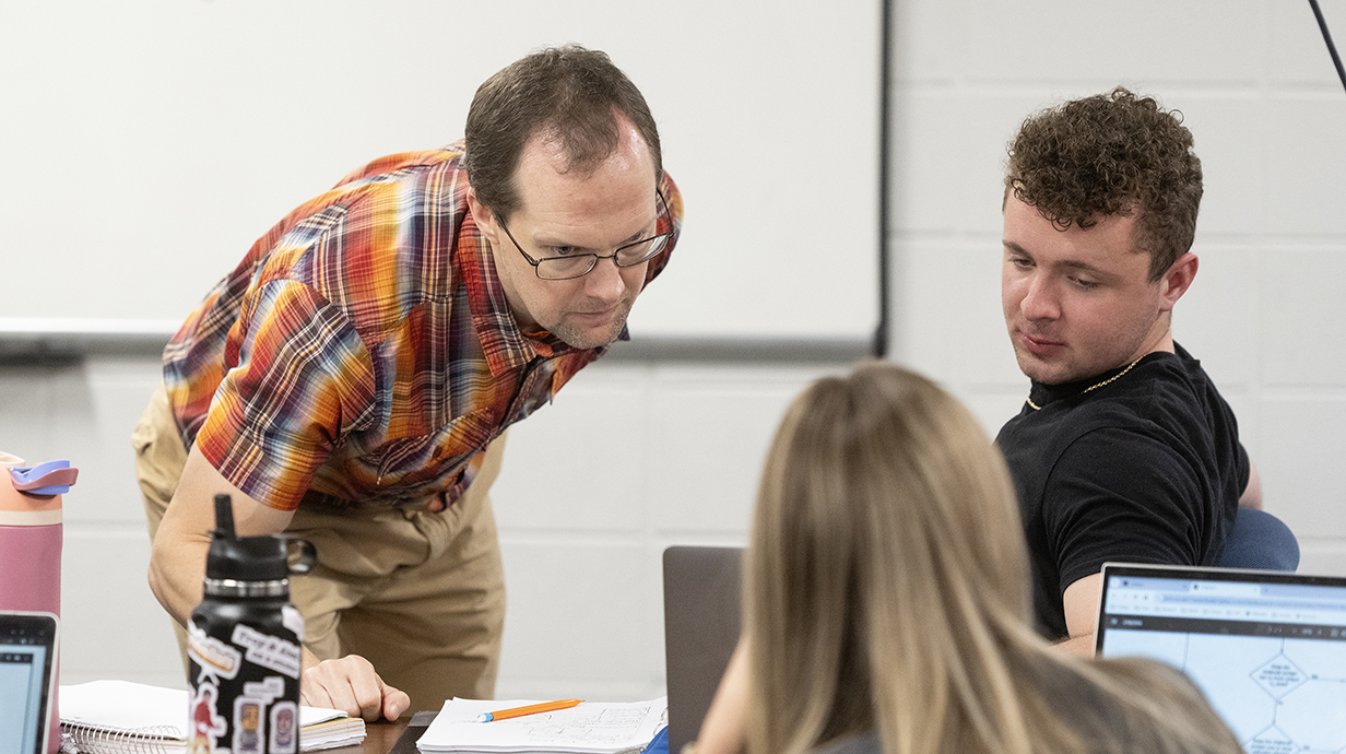 A man leans over to talk with students in a classroom.