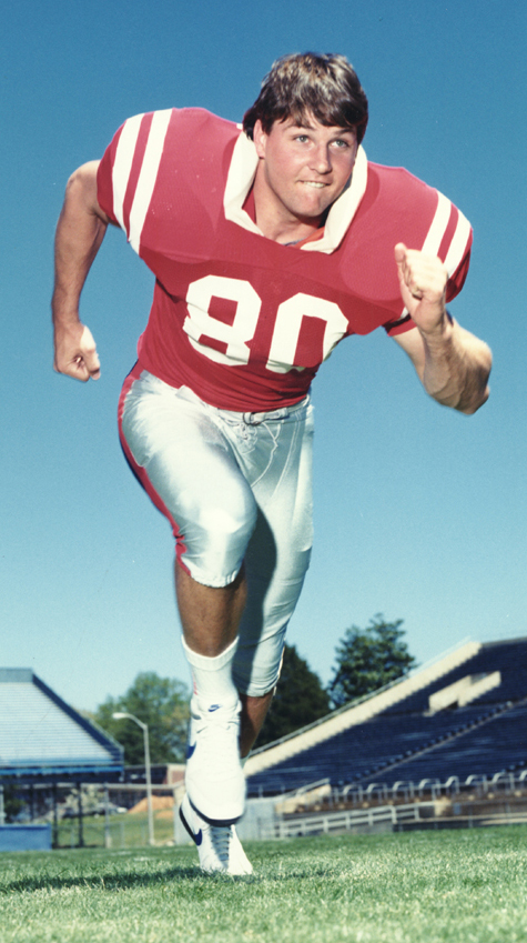 A young man wearing a red football uniform runs in a stadium.