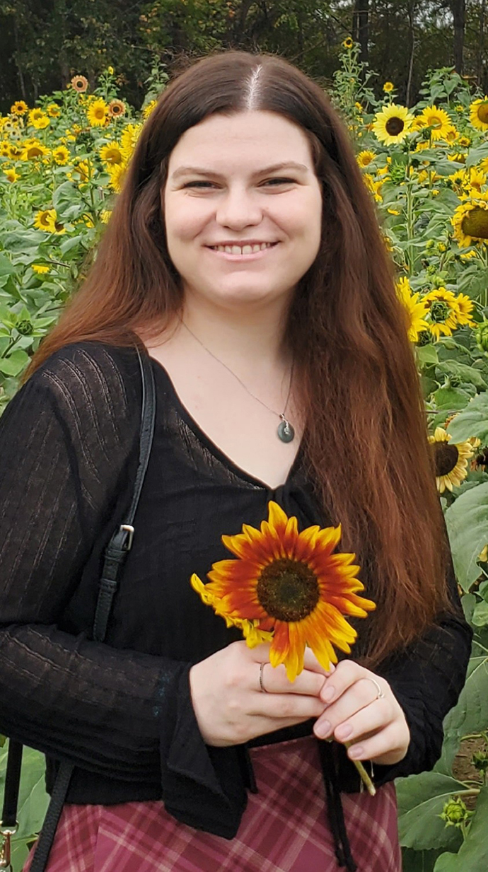 A young woman stands in a field of sunflowers holding one bloom.
