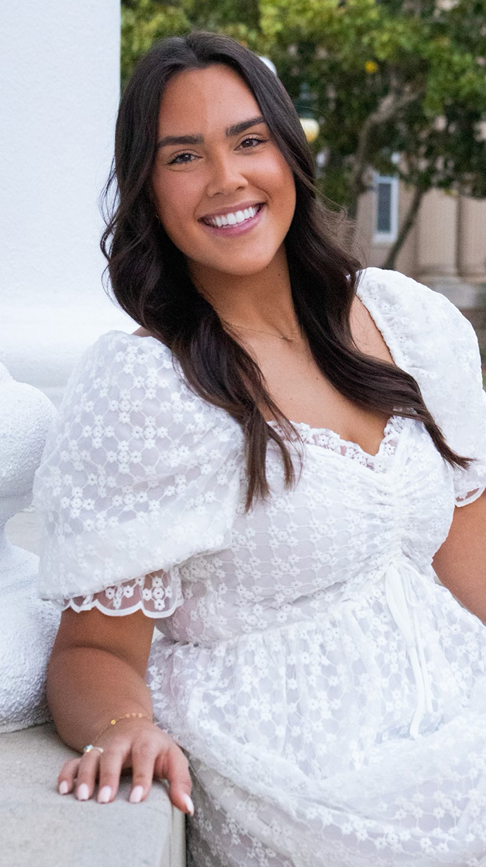 A young woman wearing a white dress leans against a white stone column.