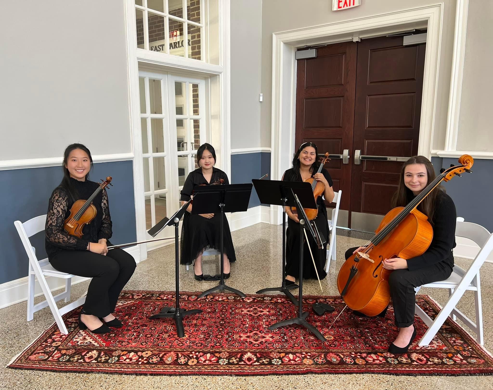Image of Linna Zheng, Keyu Zheng, Paola Betanco, and Holly Bleeden sitting in chairs holding string instruments.