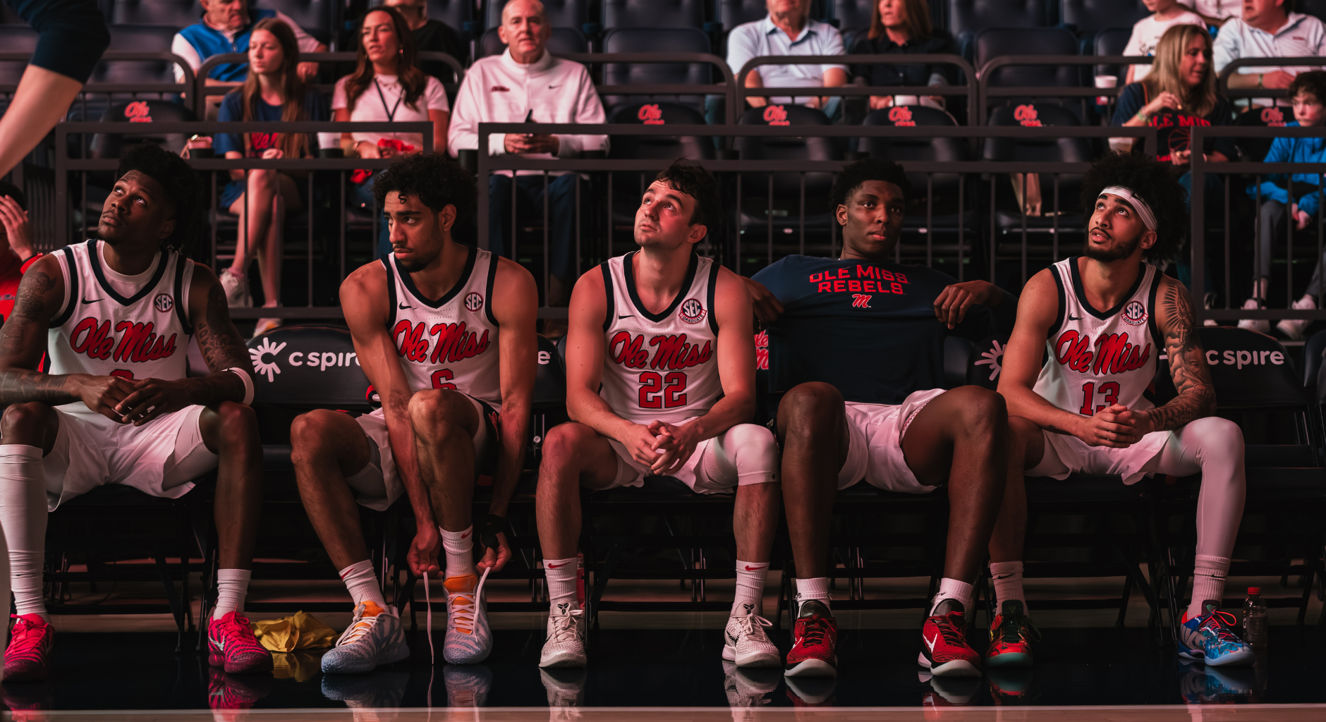 An image of five Ole Miss basketball players sitting on the bench before the start of a game.