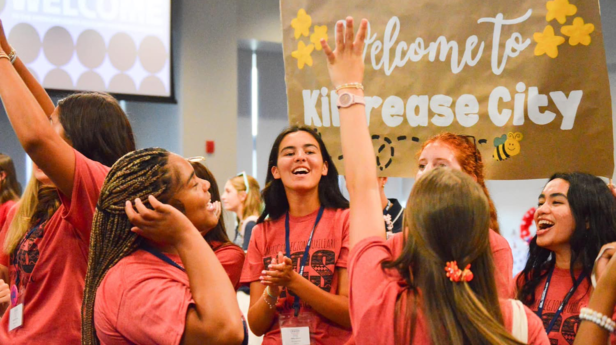 A group of young women wearing red T-shirts throw their hands up and cheer in a meeting room.