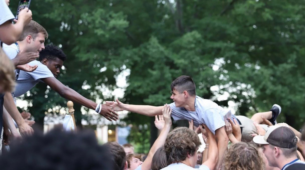 A young man crowd surfs toward a stage in a tree-lined park.
