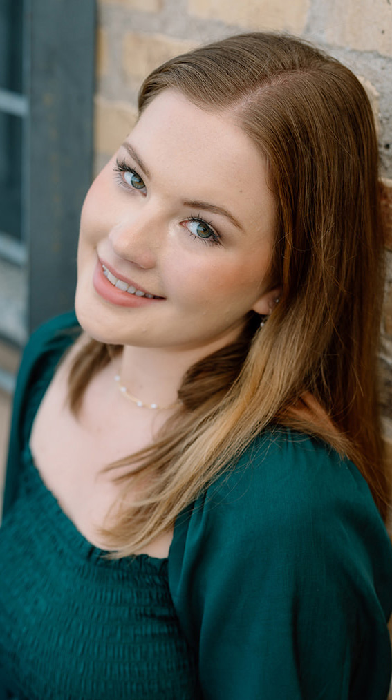 Headshot of a young woman leaning against a brick wall.