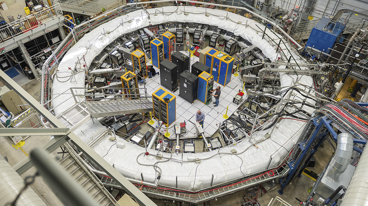 A giant electromagnet ring fills the room in a laboratory lined with electronic equipment.