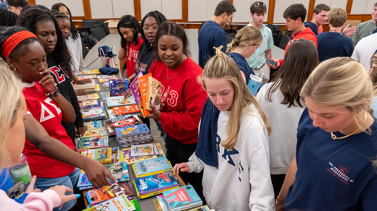 A large group of young people sort through books stacked on long tables.