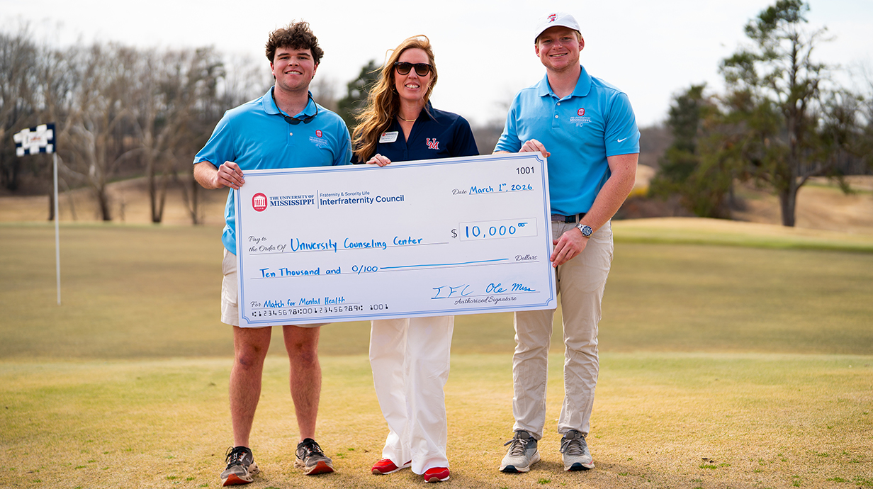 Two young men and a young woman hold a giant check for $10,000 on a golf course.