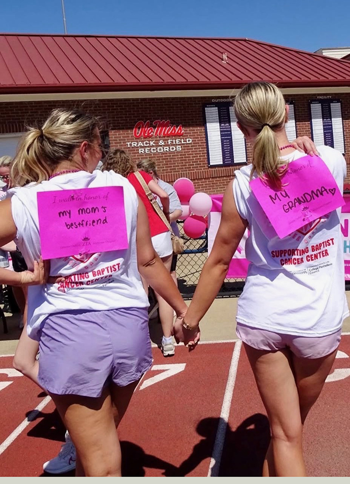 Two young women walk on a track wearing bright pink signs on their backs.