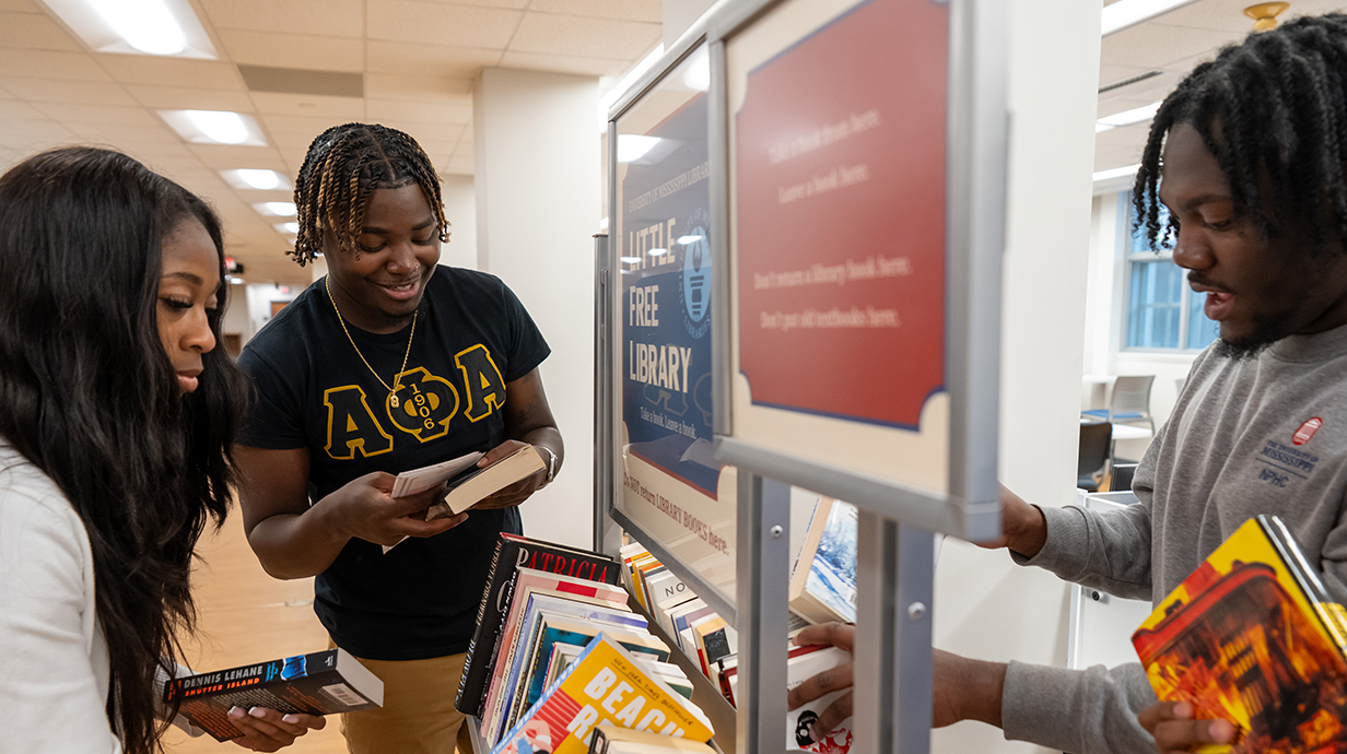 Three young people sort books into a standing bin.