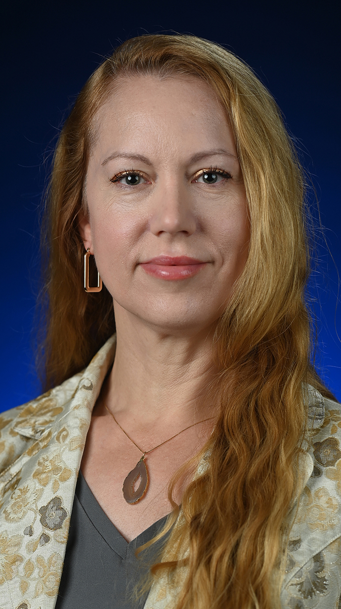Headshot of a woman wearing a light-colored leaf-print jacket over a gray blouse.