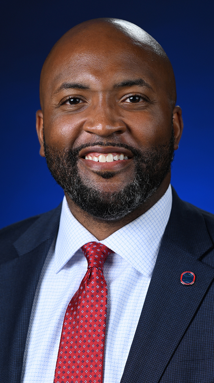 Headshot of a man wearing a dark suit with a red tie.