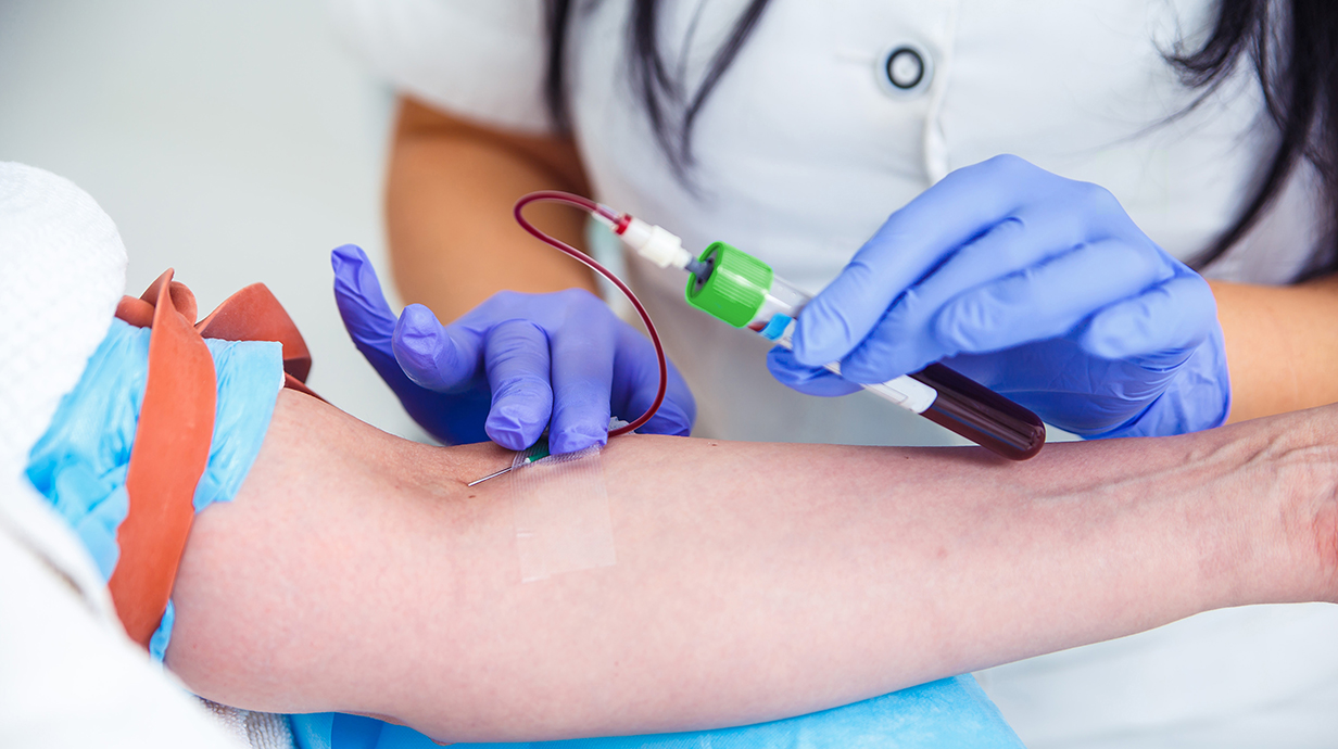 A medical professional draws blood from a patient's arm.