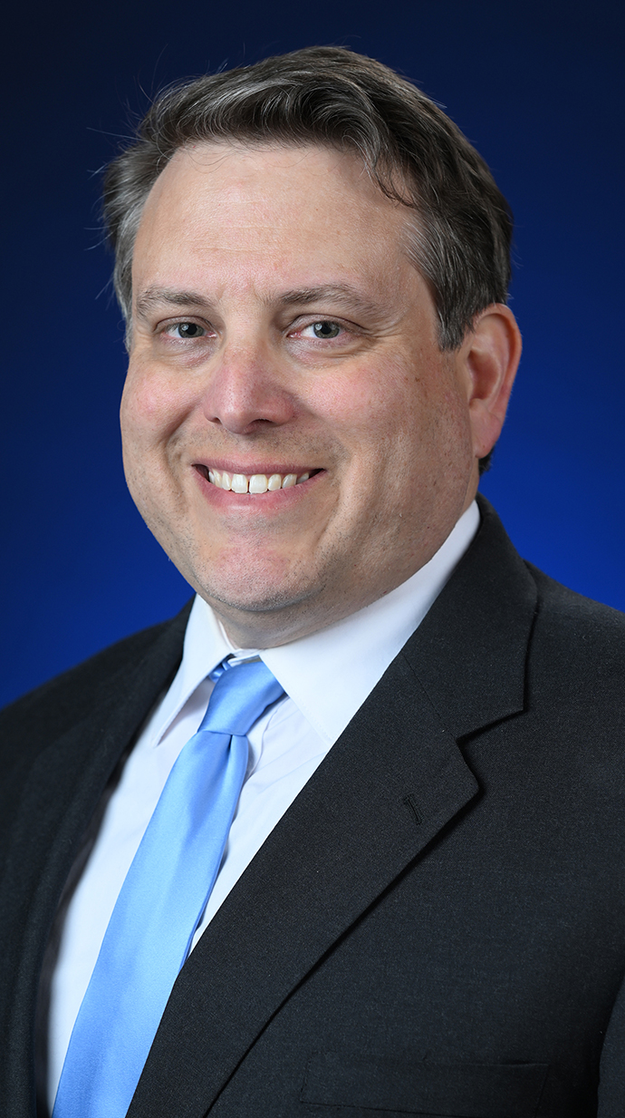 Headshot of a man wearing a dark suit and a light blue tie.