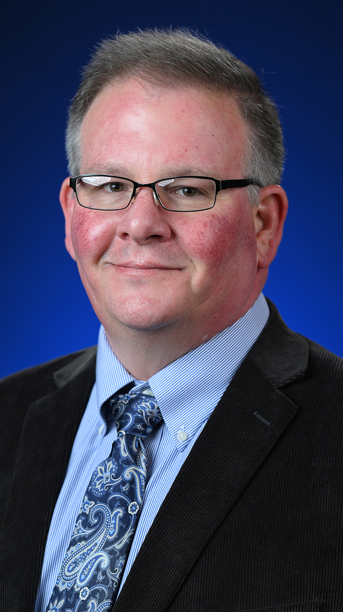 Headshot of a man wearing glasses and a dark suit.