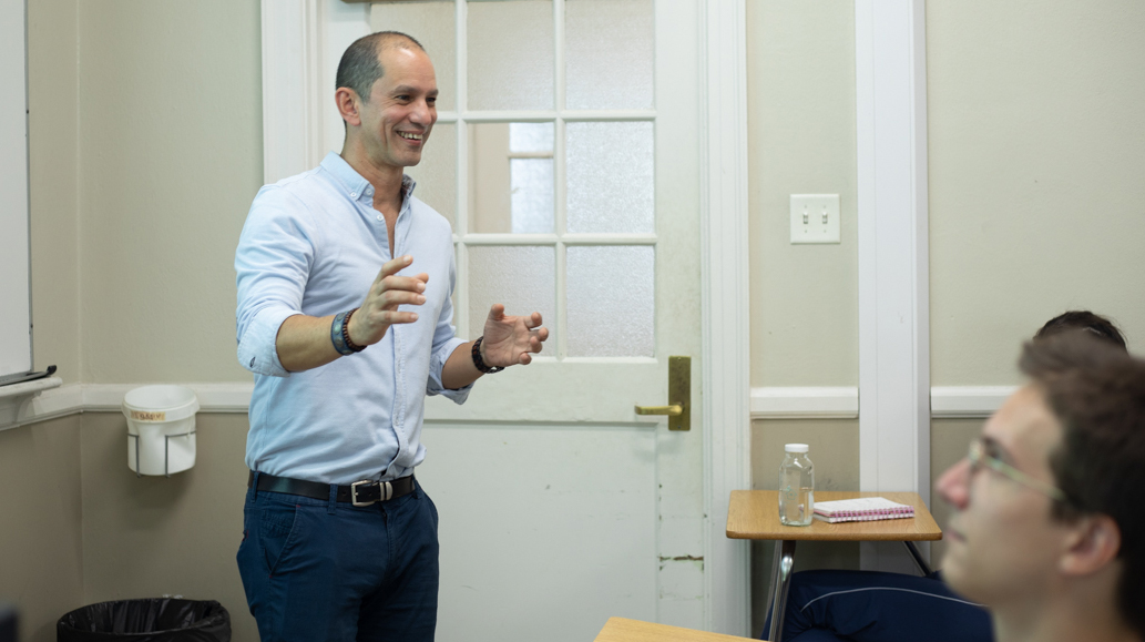 A man gestures as he talks to students in a classroom.