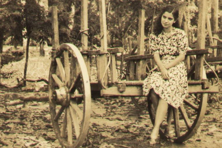 A sepia-toned photo of a young woman sitting on the back of a wooden wagon.