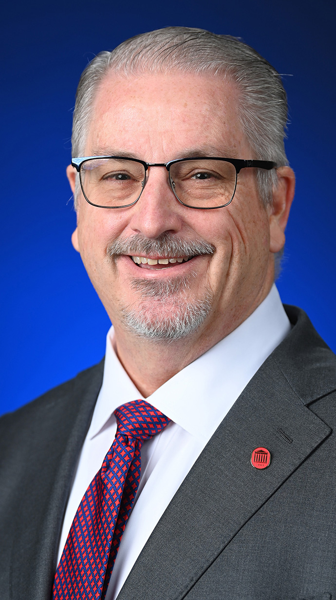 Headshot of a man wearing a gray suit and a red tie.