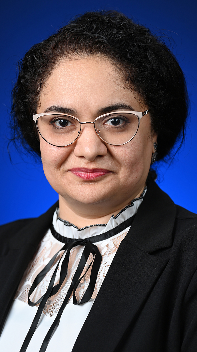 Headshot of a woman wearing a black jacket over a white blouse tied with a black ribbon.