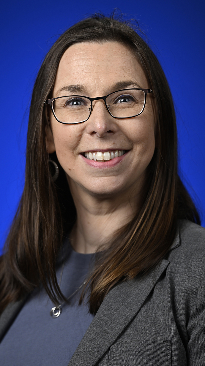 Headshot of a woman wearing a gray jacket over a dark blue blouse.