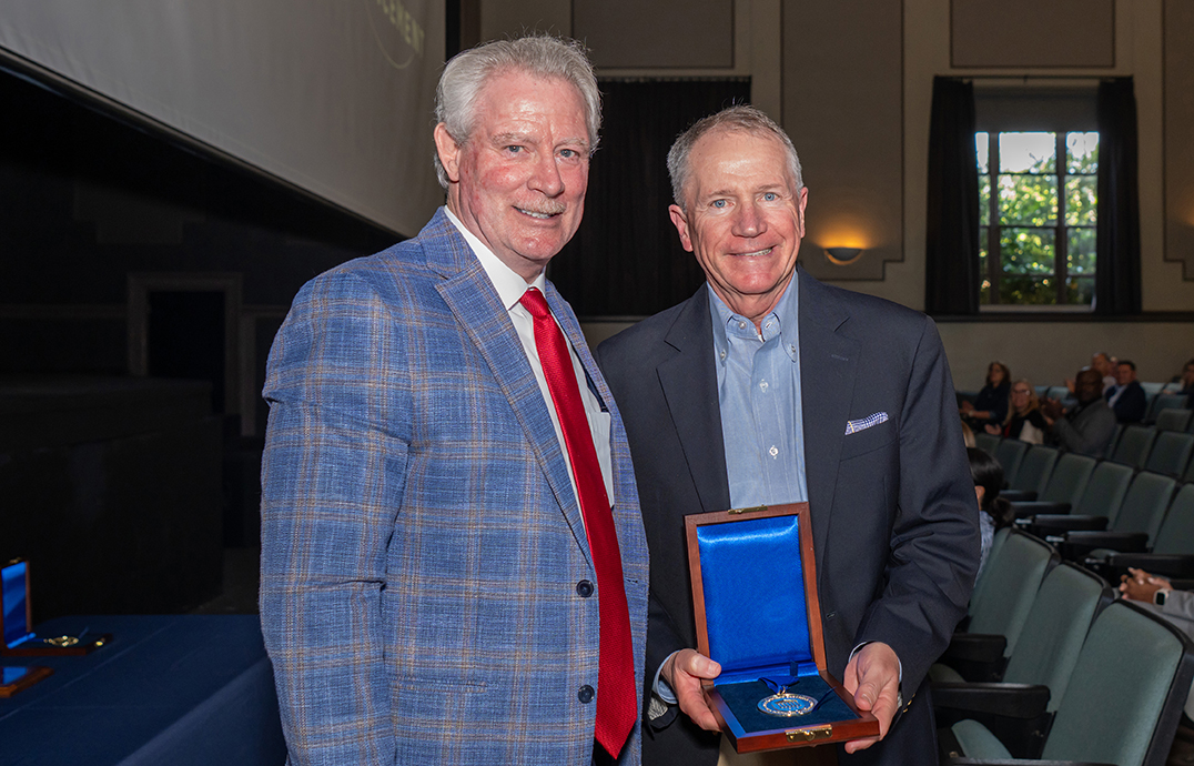Photo of a man presenting a medal to another man in an auditorium.