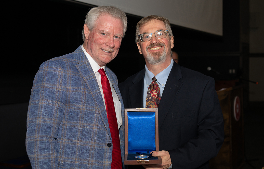 A man presents a medal to another man in an auditorium.