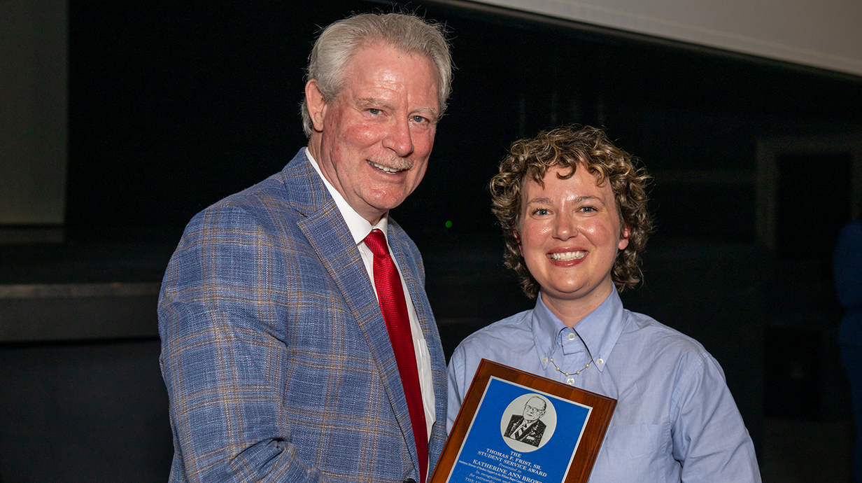 A man wearing a suit presents a woman with an award plaque in an auditorium.