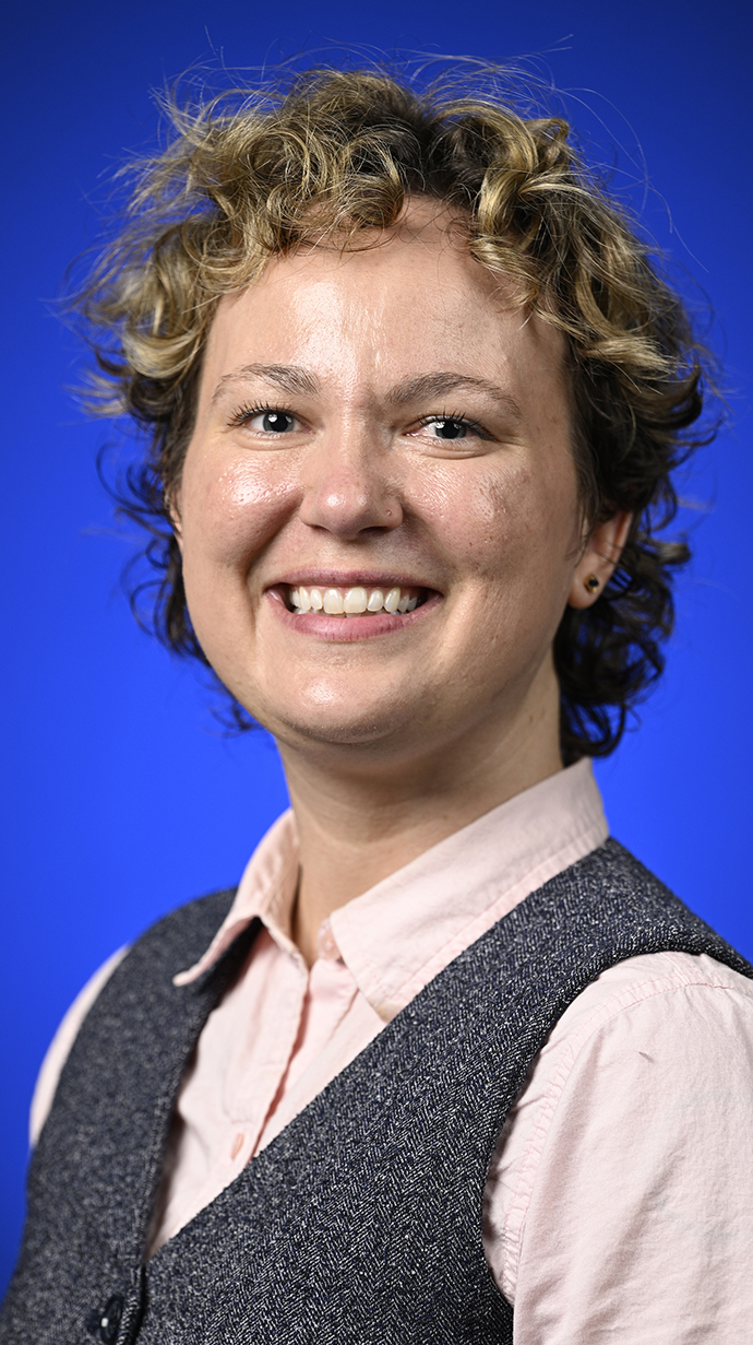 Headshot of a woman wearing a gray vest over a pink shirt.