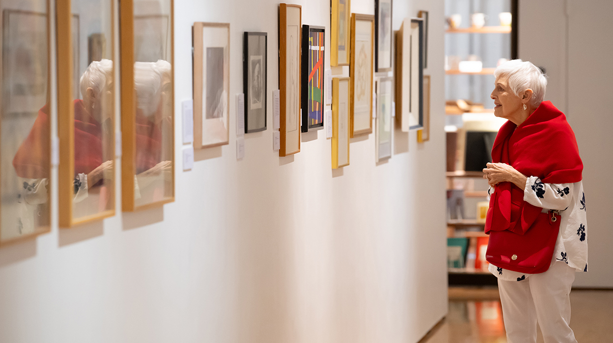 A woman looks at a line of paintings hanging in a gallery.