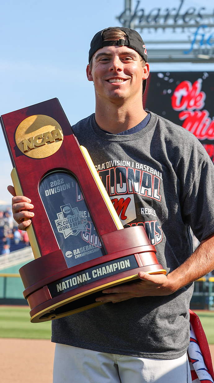 A baseball player holds a championship trophy in a stadium.