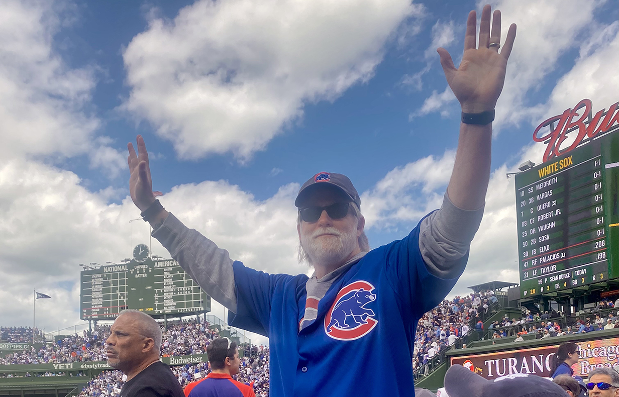 A man wearing a Chicago Cubs jersey stands in the seating area of a baseball stadium.