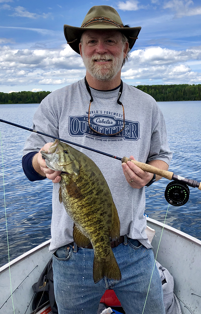 A man standing in a boat holds a large fish he has caught.