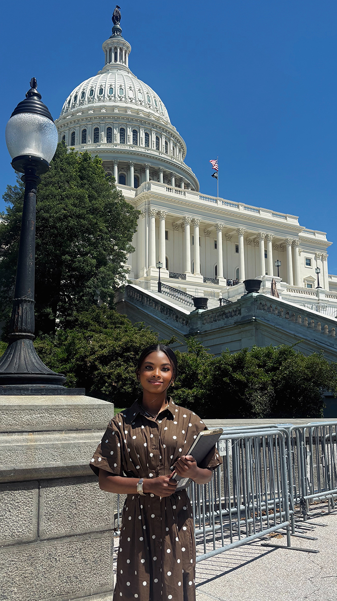 A young woman holding a clipboard stands in front of the U.S. Capitol.
