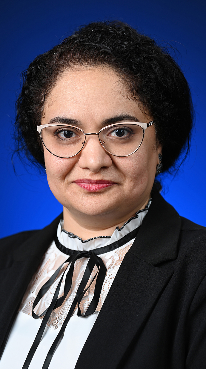Headshot of a woman wearing a black jacket over a white blouse with a black string tie.