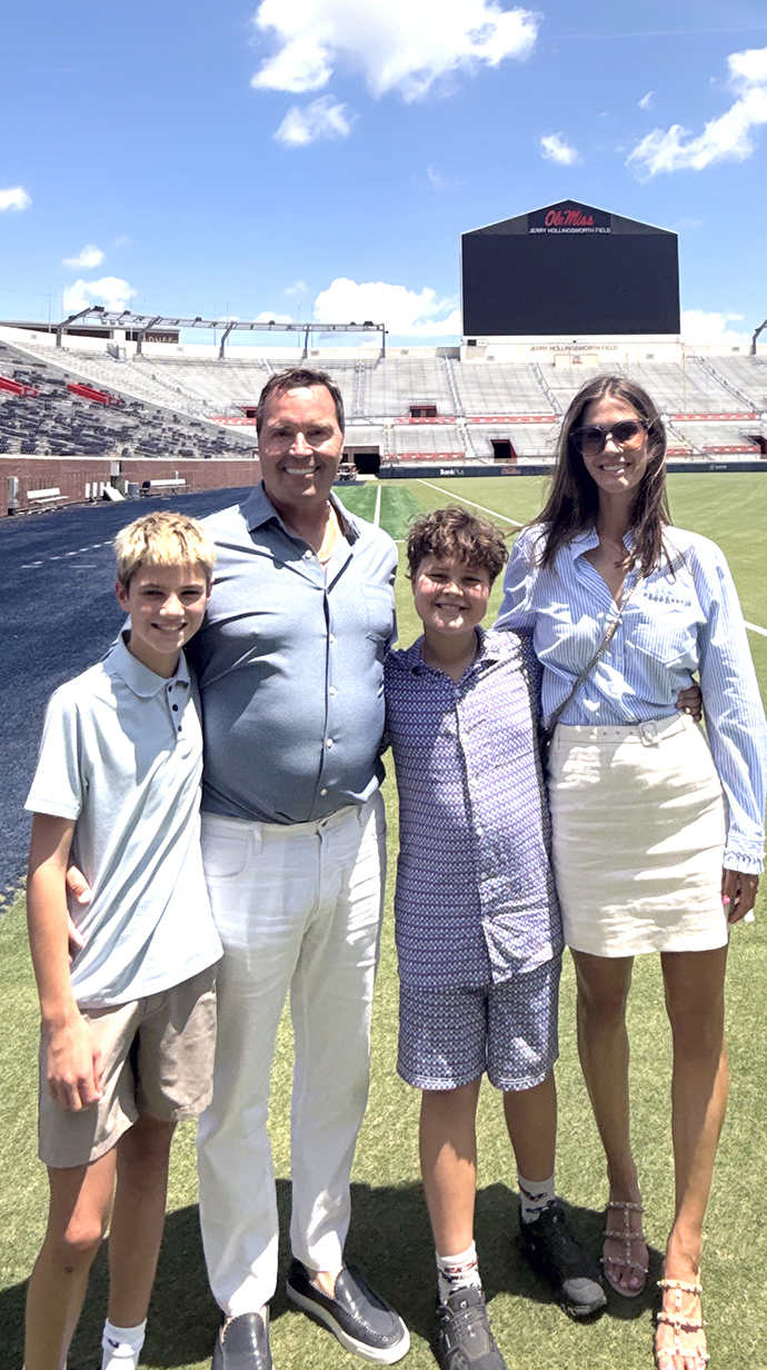 A man, a woman and two boys stand on the field in an empty football stadium.