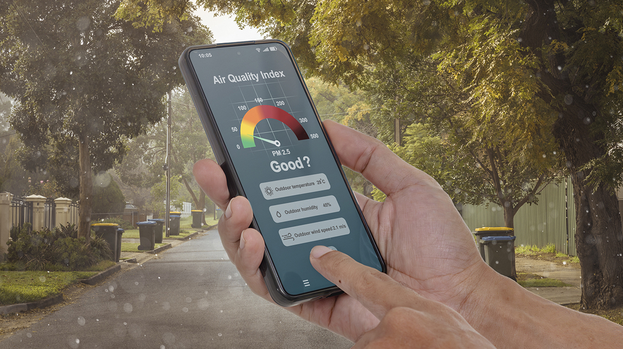 Photo illustration of a hand holding a cellphone displaying an air quality monitor that questions whether the levels are safe.