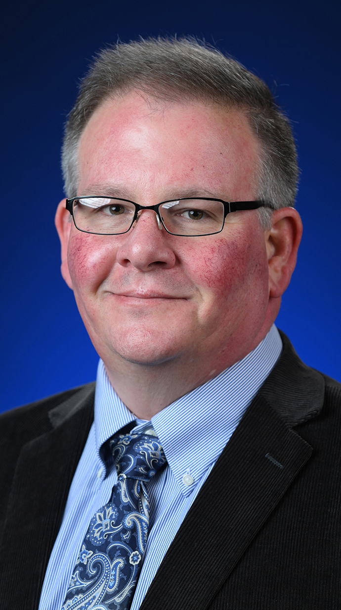 Headshot of a man wearing a dark suit with a blue paisley tie.