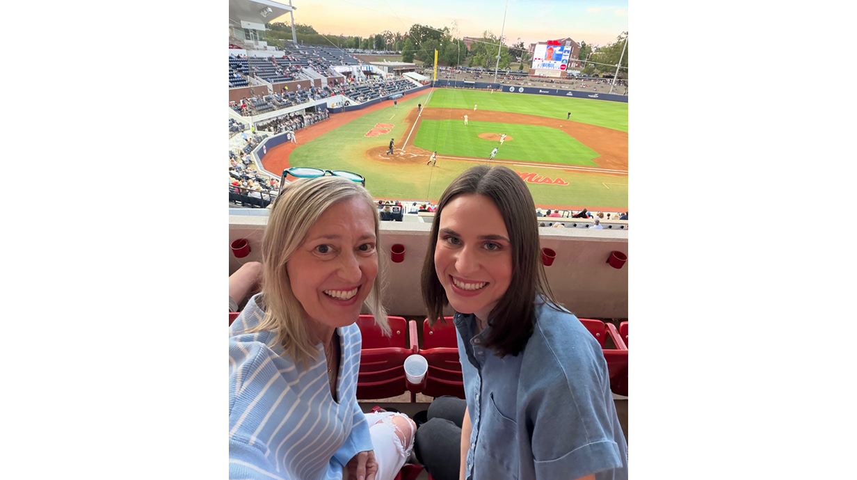 Two women sit in a baseball stadium during a game.