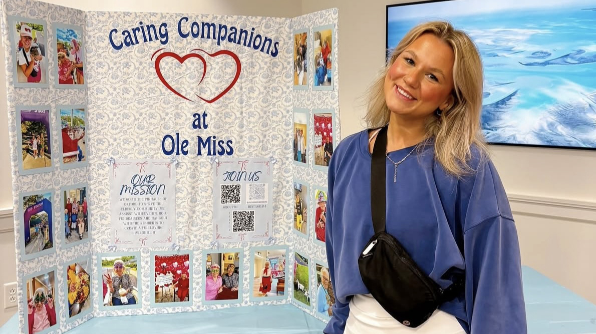A young woman stands with a posterboard reading 'Caring Companions.'