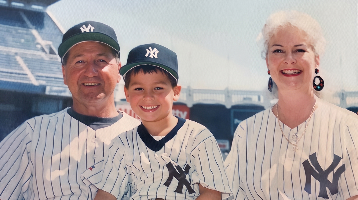 A man, a young boy and a woman, all wearing New York Yankees jerseys, stand in a stadium.