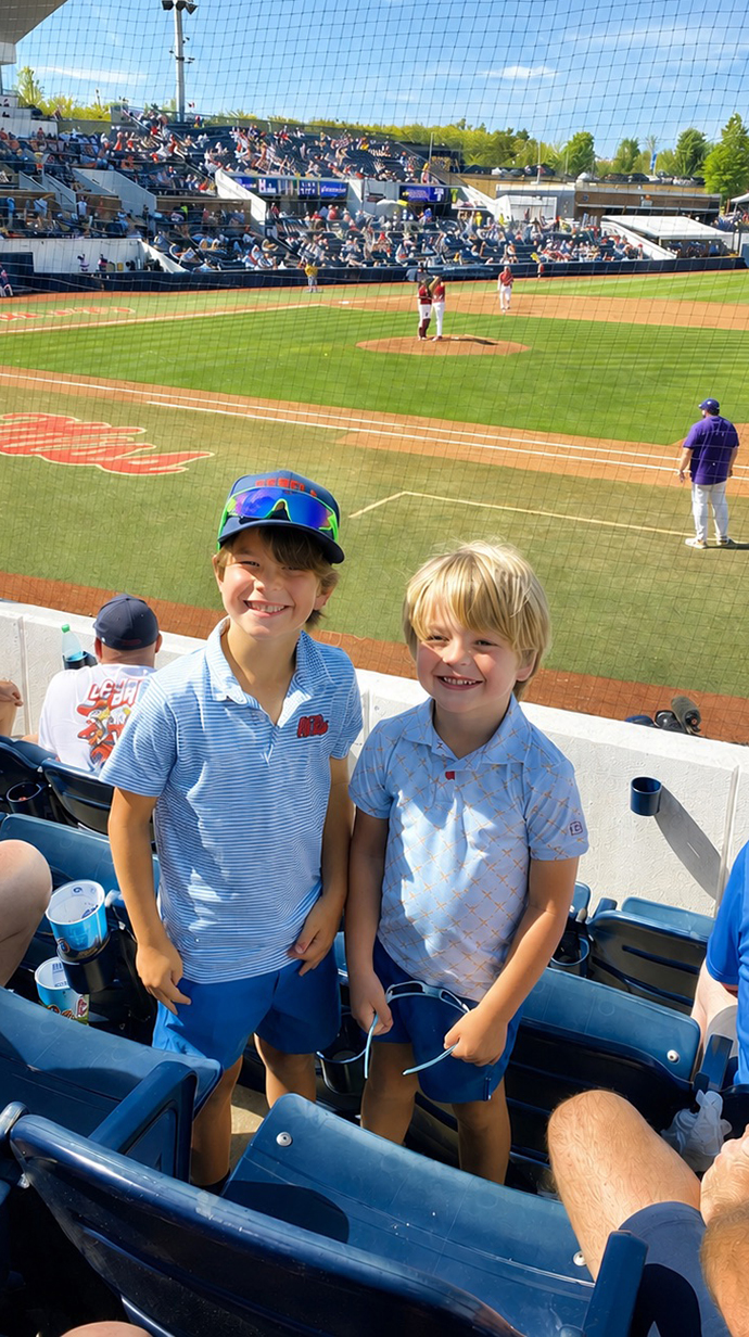 Two small boys stand in the seating area of a baseball stadium.