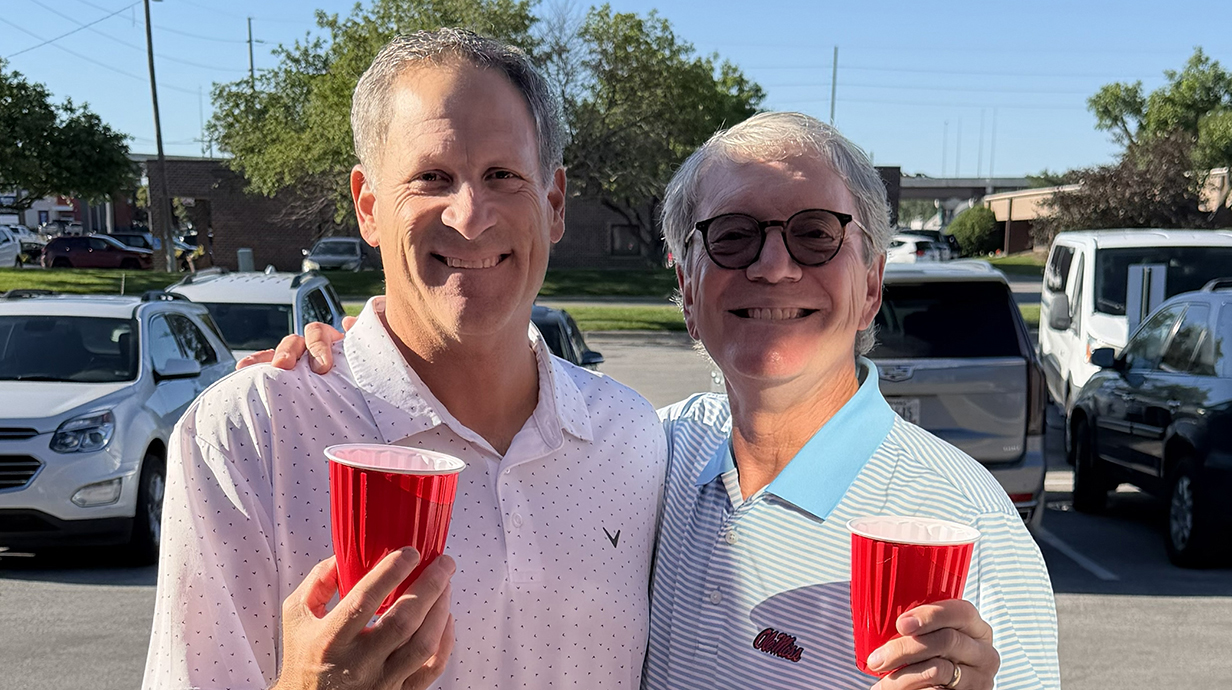 Two men holding red plastic cups stand in a parking lot.