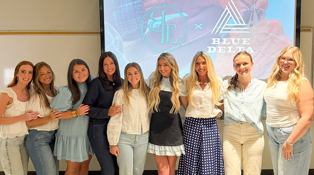 A group of young women stand in front of a projection screen in a classroom.