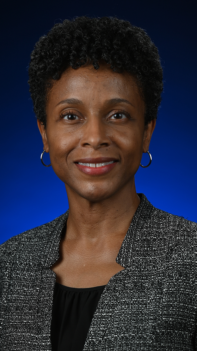 Headshot of a woman wearing a gray jacket over a black blouse.