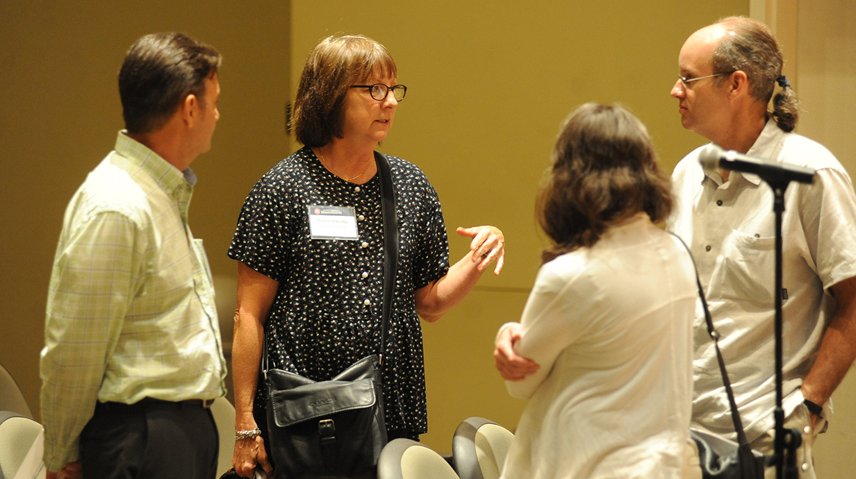 Two men and two women chat in an auditorium.