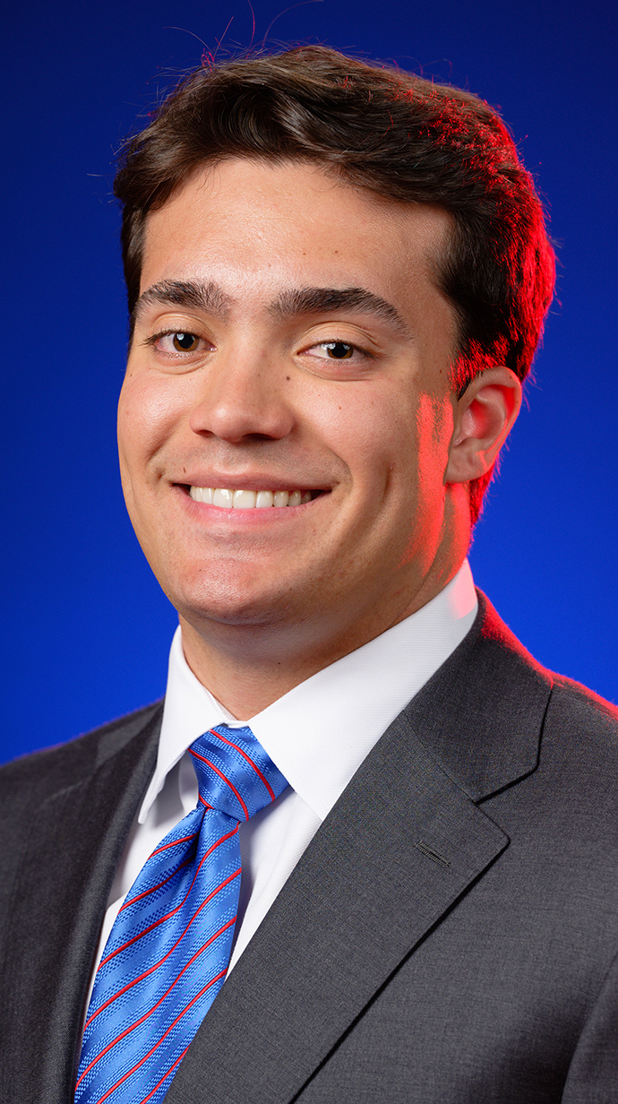 Headshot of a young man wearing a dark suit with a blue tie.
