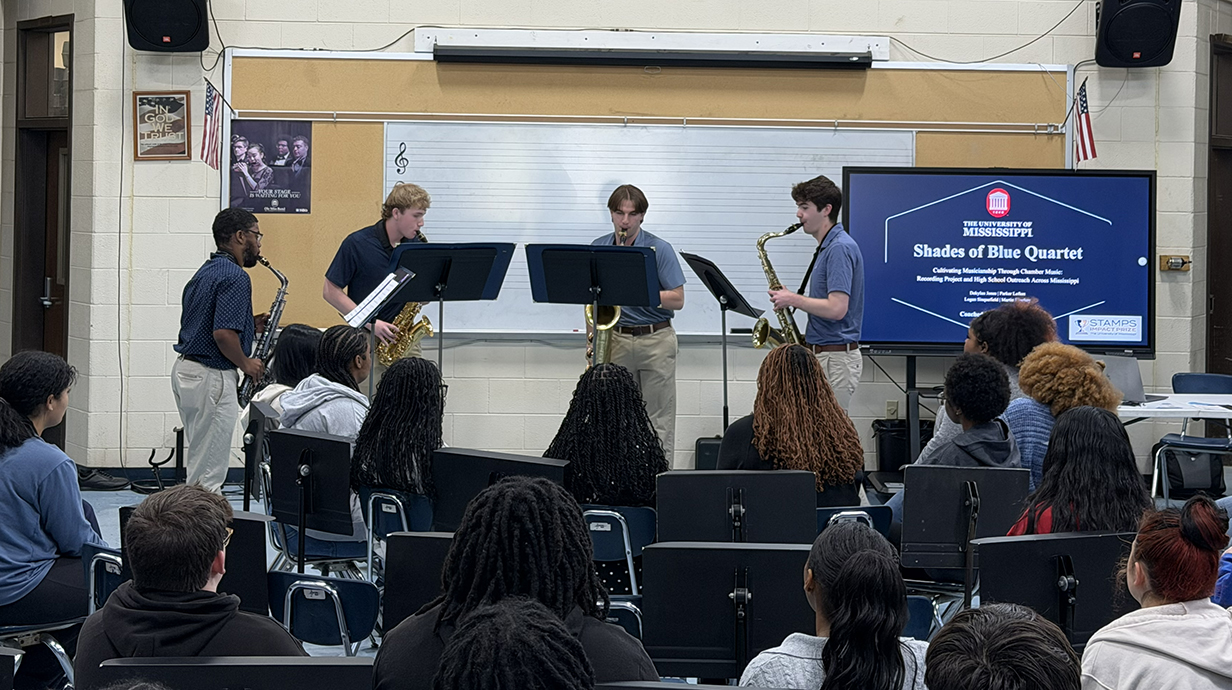 Four young men play saxophones at the front of a classroom.