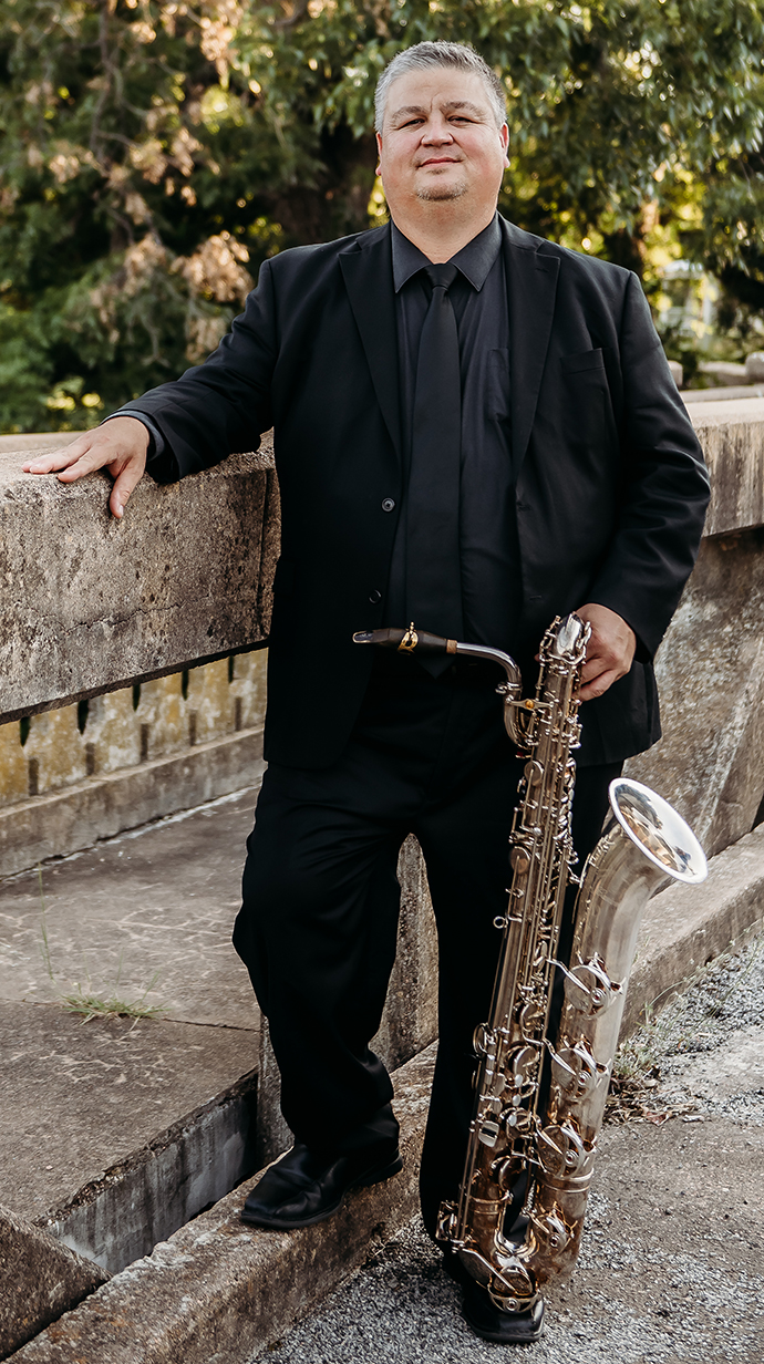 A man holds a large saxophone while standing on a concrete landing.