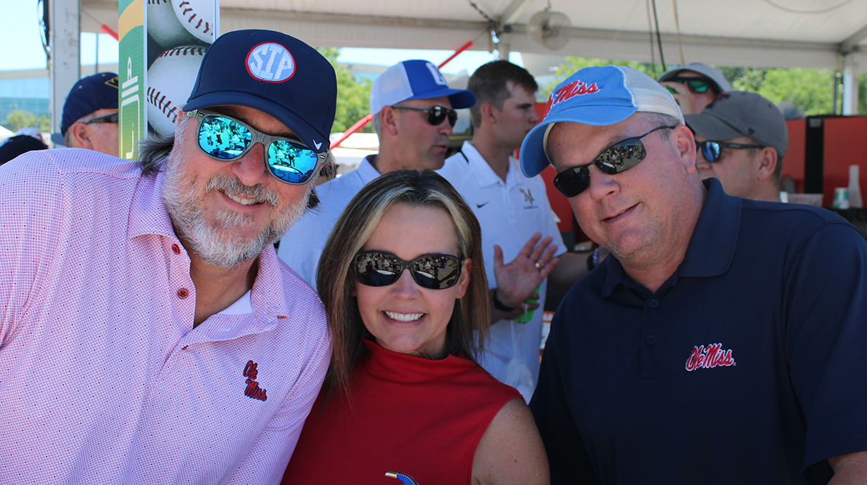 A large group of people wearing Ole Miss gear stand underneath an outdoor pop-up tent.