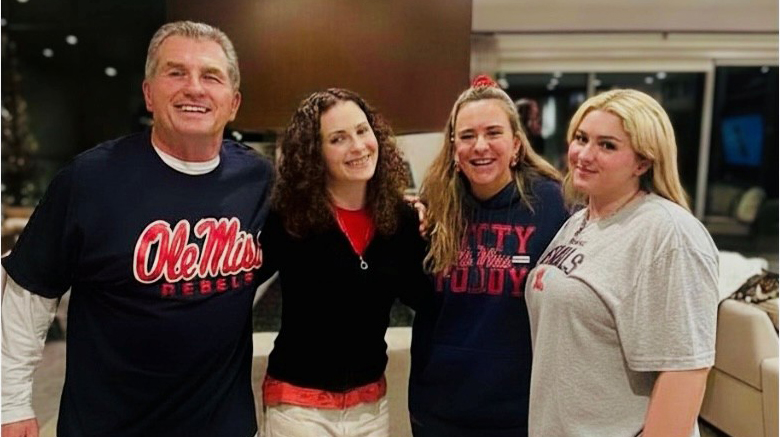 A man and three women, all wearing Ole Miss apparel, stand in a lobby.